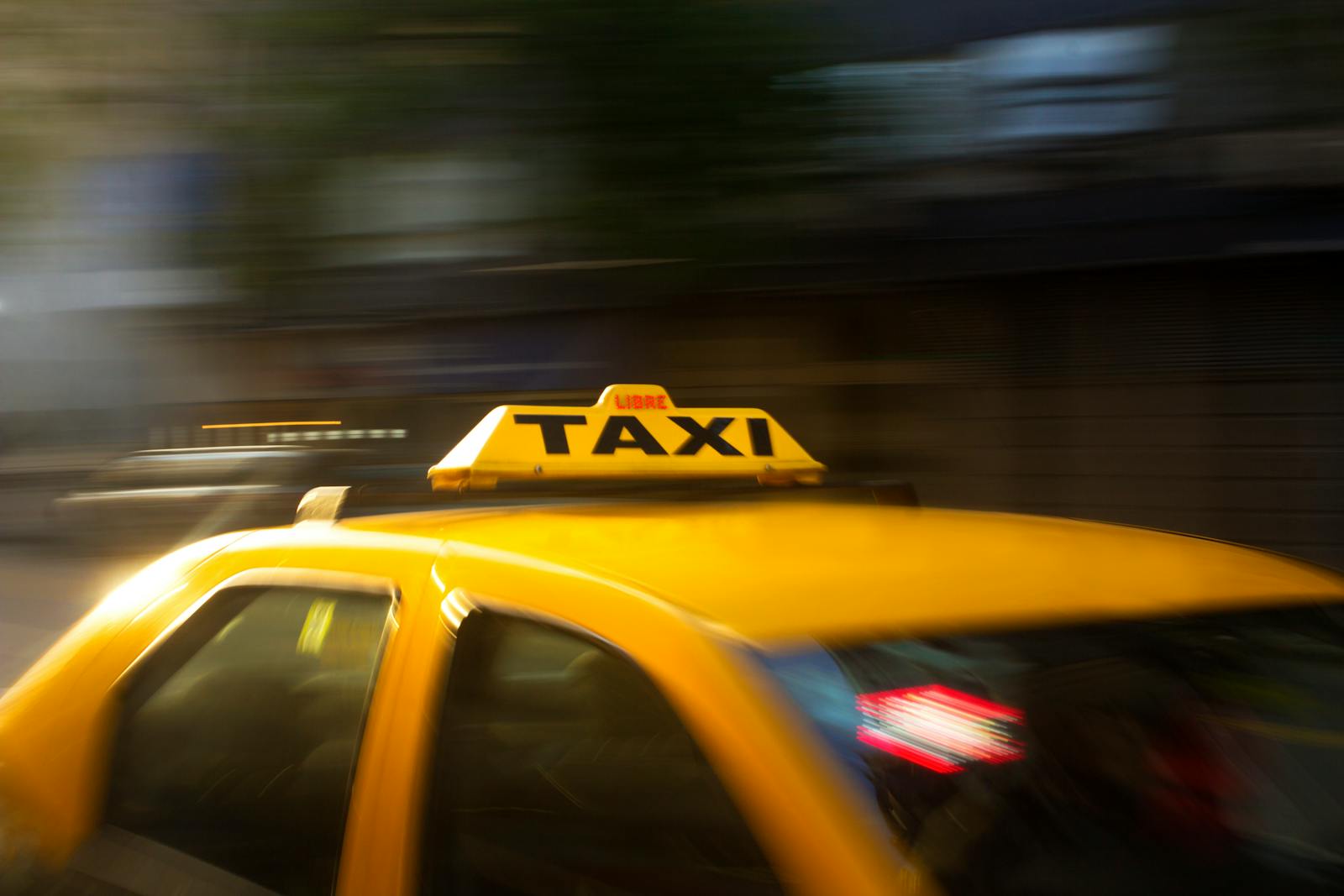 A vibrant yellow taxi with motion blur speeding through a nighttime city street.